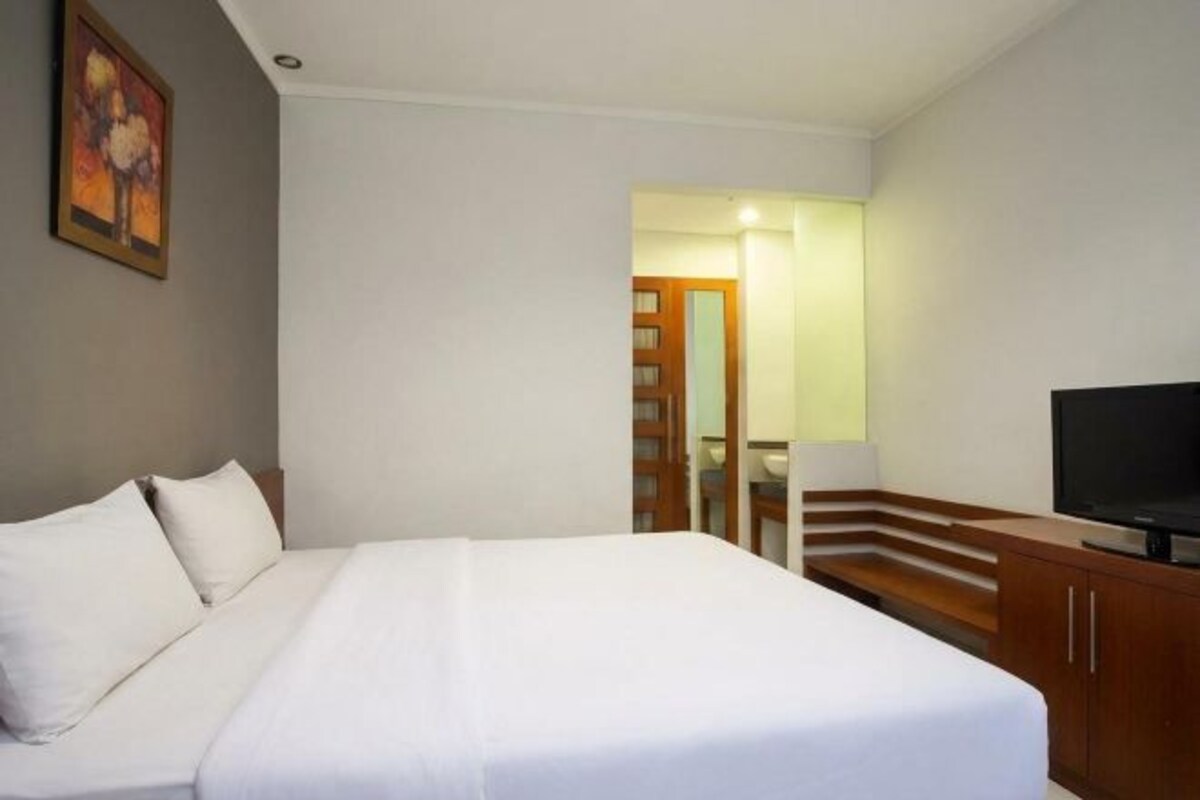 A hotel room with a bed, a television, and a wooden cabinet.