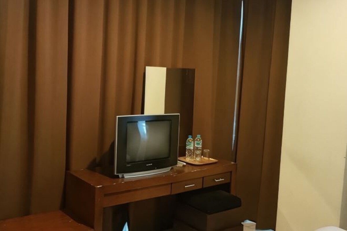 A hotel room with a TV on a wooden desk, a mirror, and a small table with two bottles.