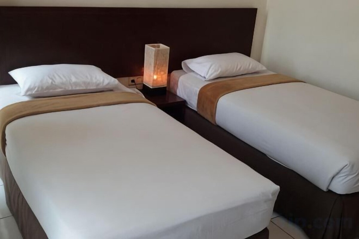 Ein Hotelzimmer mit zwei Einzelbetten, einem Nachttisch und einer Nachttischlampe.