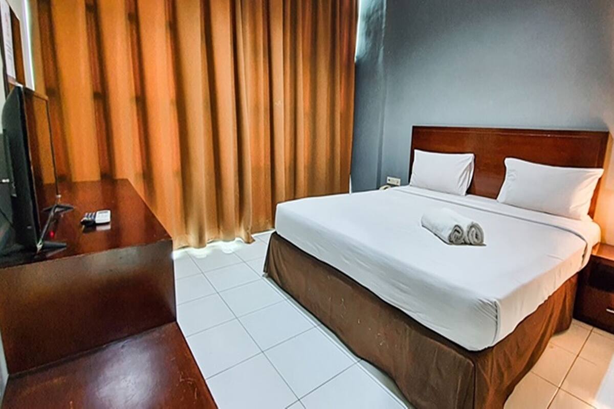 Een hotelkamer met een bed, bureau, stoel, televisie en lamp.