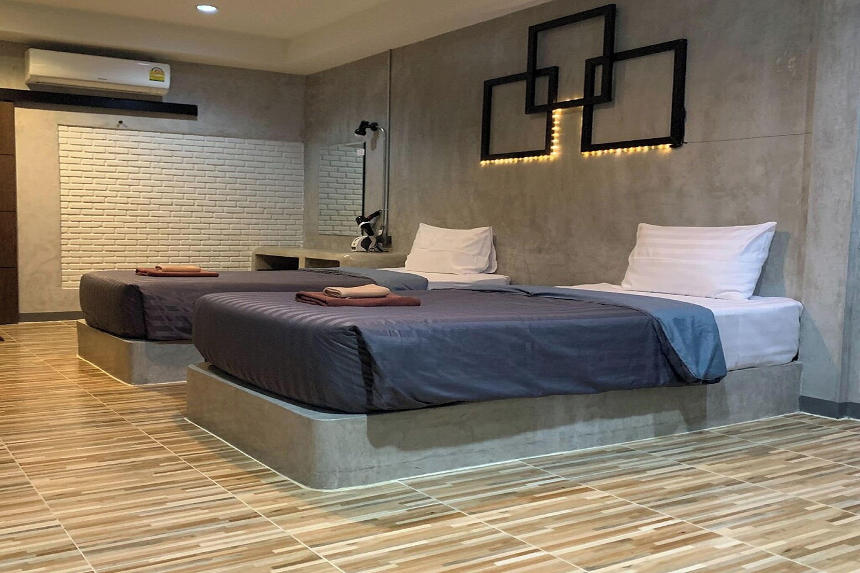 A modern hotel room with two beds, a large mirror, and a wall-mounted air conditioner.