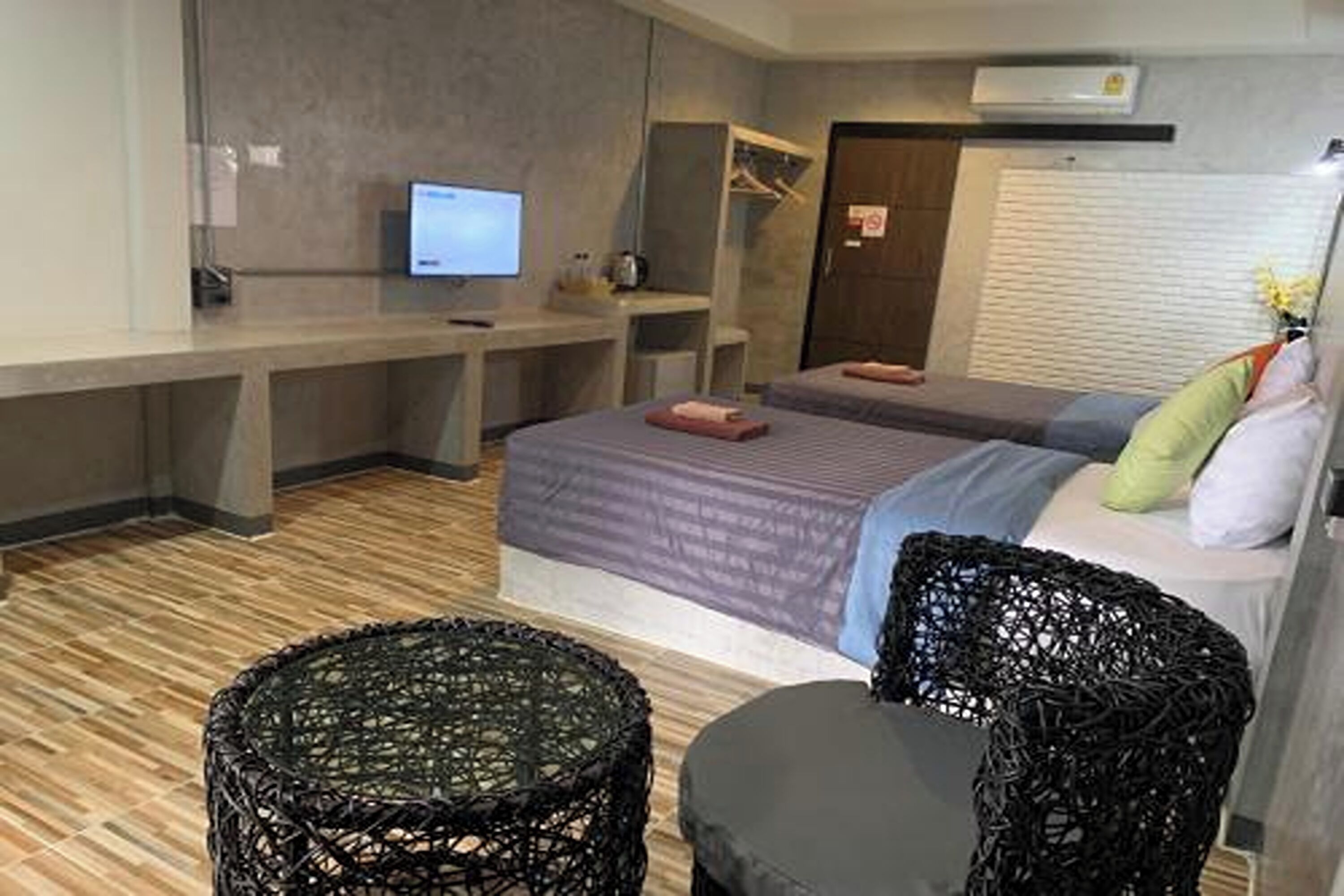 Quarto de hotel moderno com cama, duas mesinhas de cabeceira, escrivaninha, cadeira e televisão.
