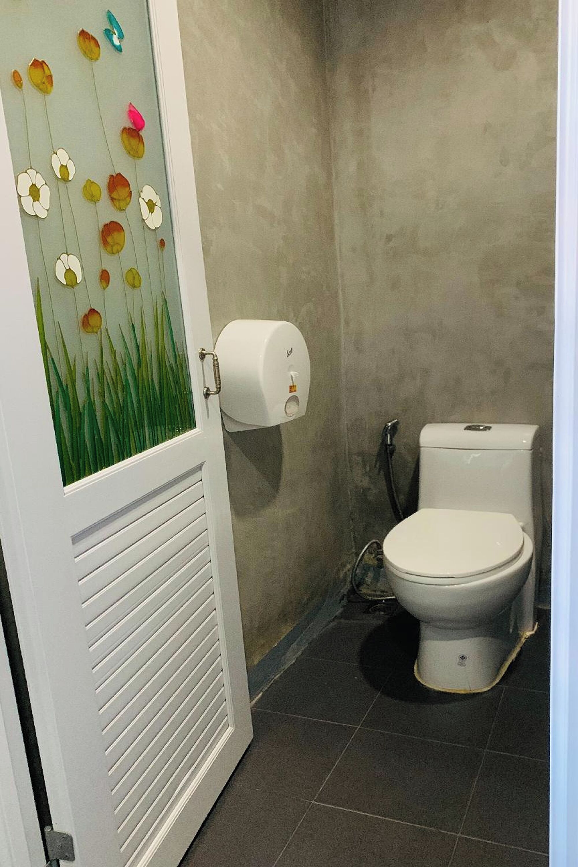 A bathroom with a toilet, a paper towel dispenser, and a door with a floral design.