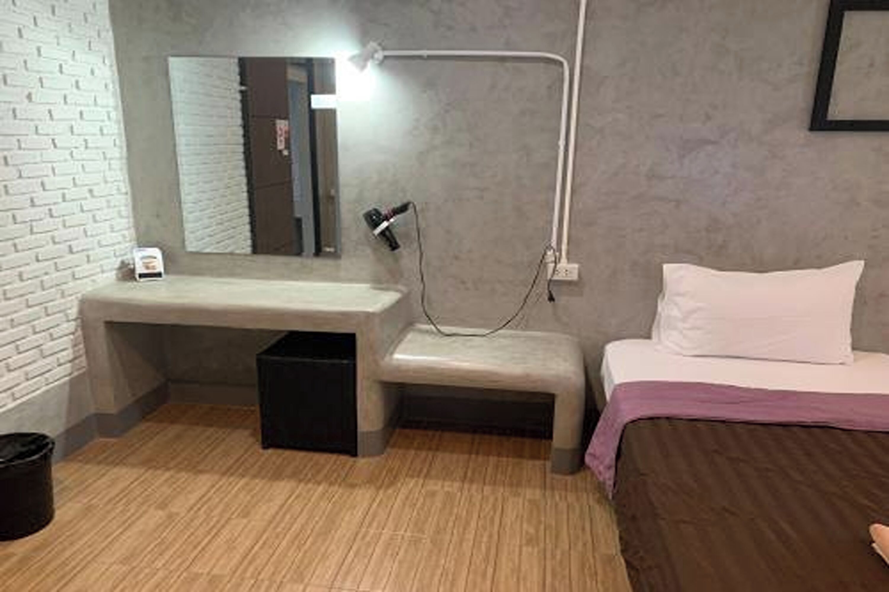 A compact hotel room with a single bed, a small bench, a bedside table, a mirror, and a hairdryer.