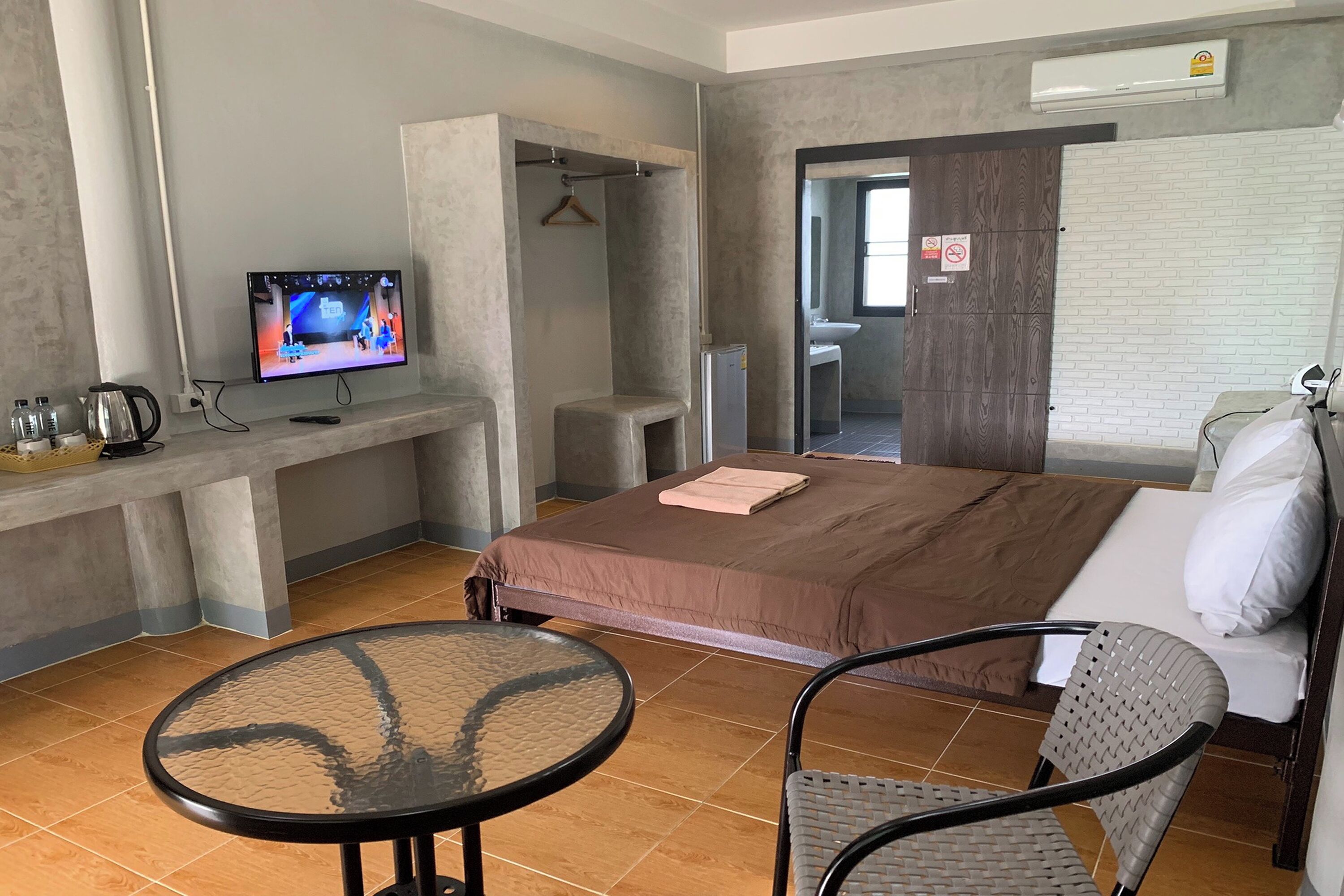 Una habitación de hotel con cama, televisión, una mesita, una silla y un baño visible a través de una puerta abierta.