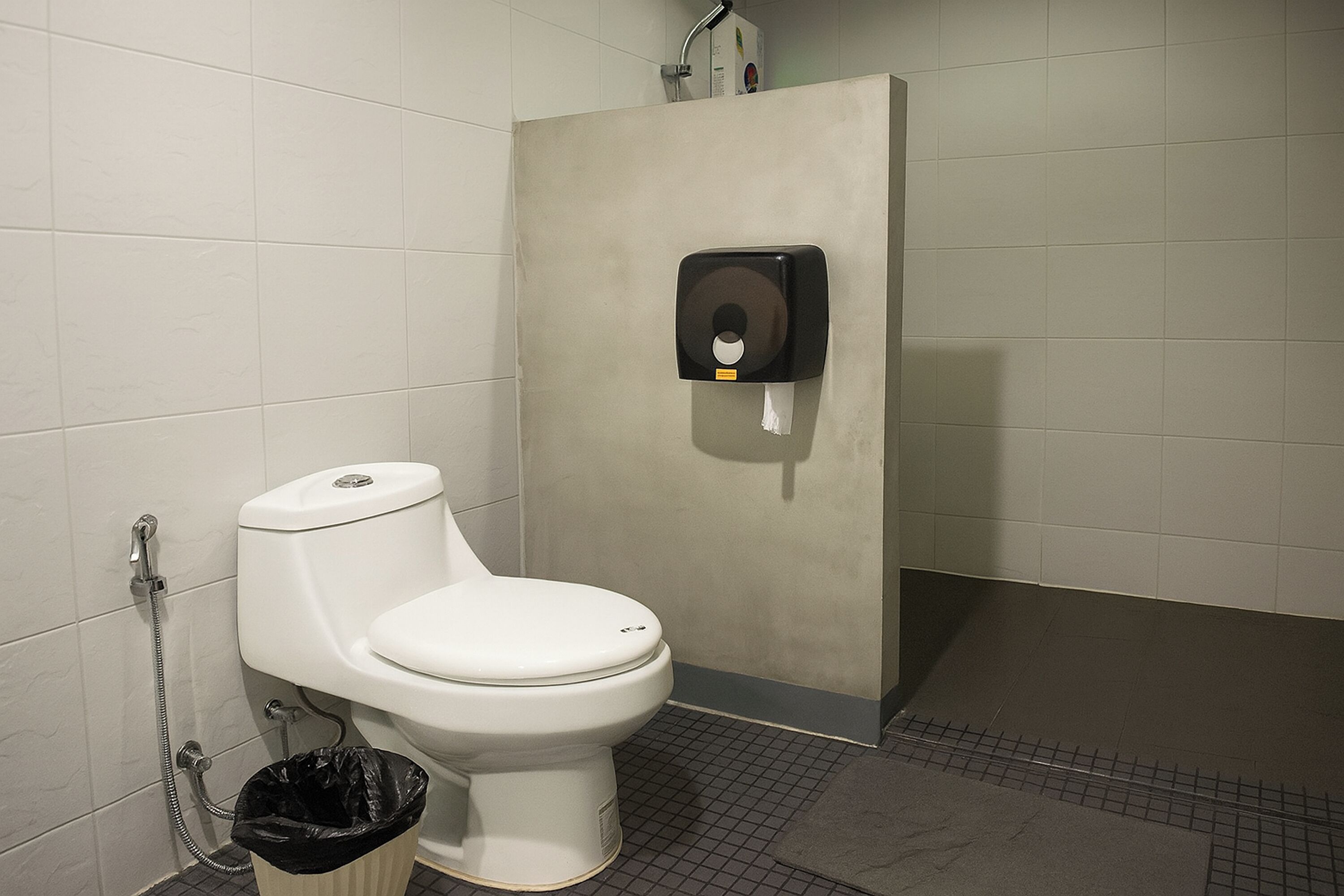 Un baño con inodoro blanco, un bote de basura negro y un dispensador de toallas de papel en la pared.