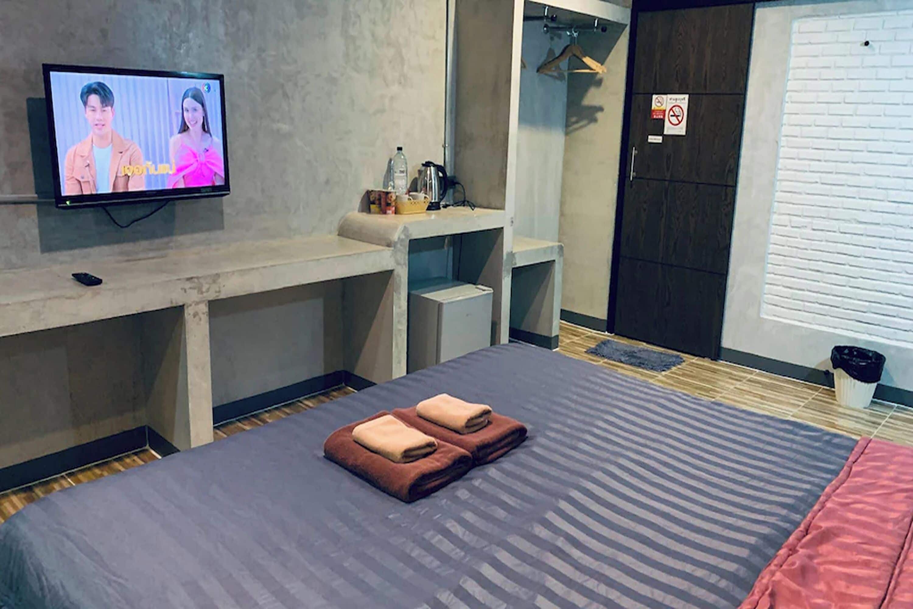 Een hotelkamer met een bed, een tv waarop een programma draait, een bureau en een kledingkast.