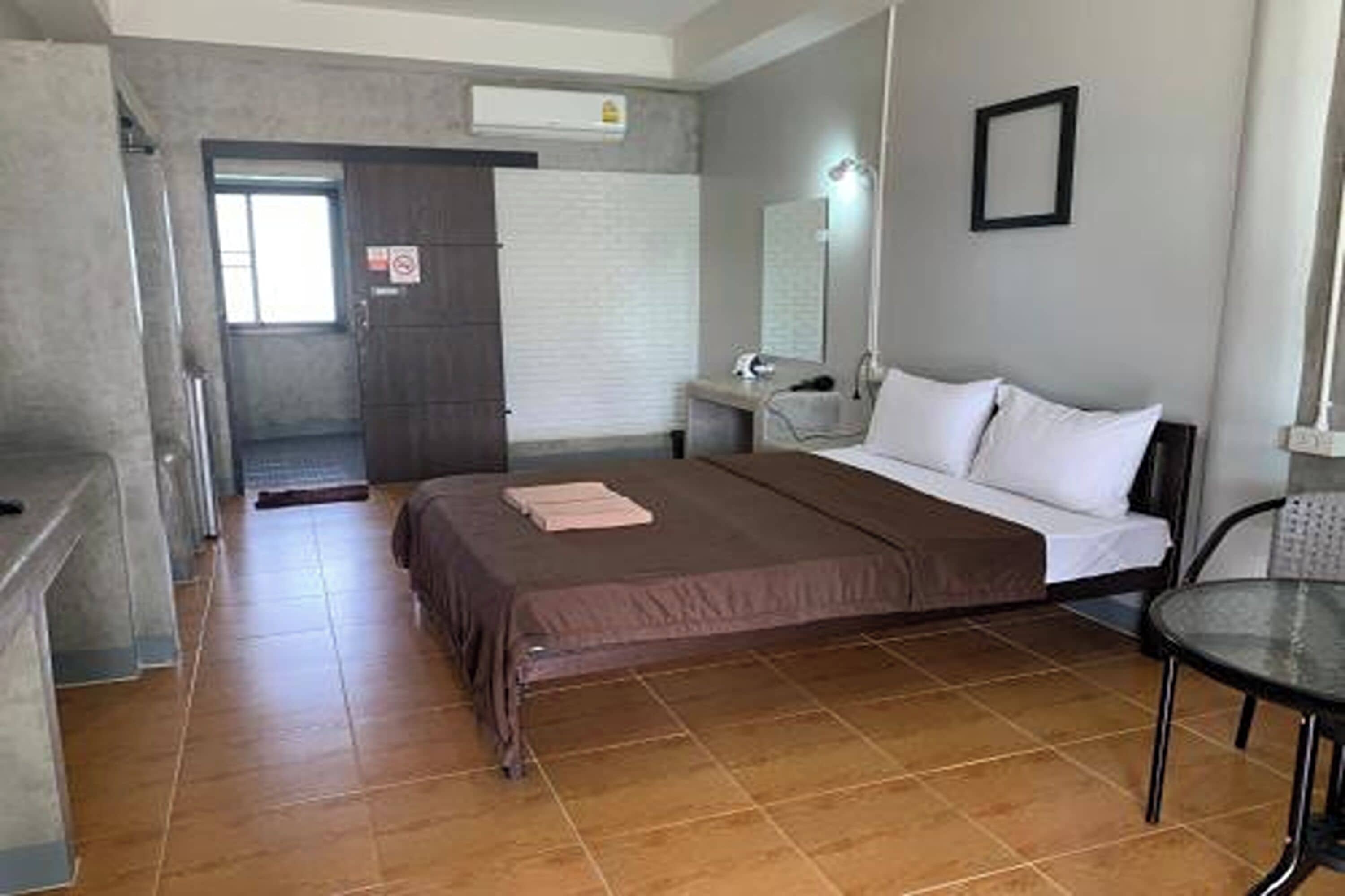 A bedroom with a bed, a bedside table, a chair, a window, and a door.