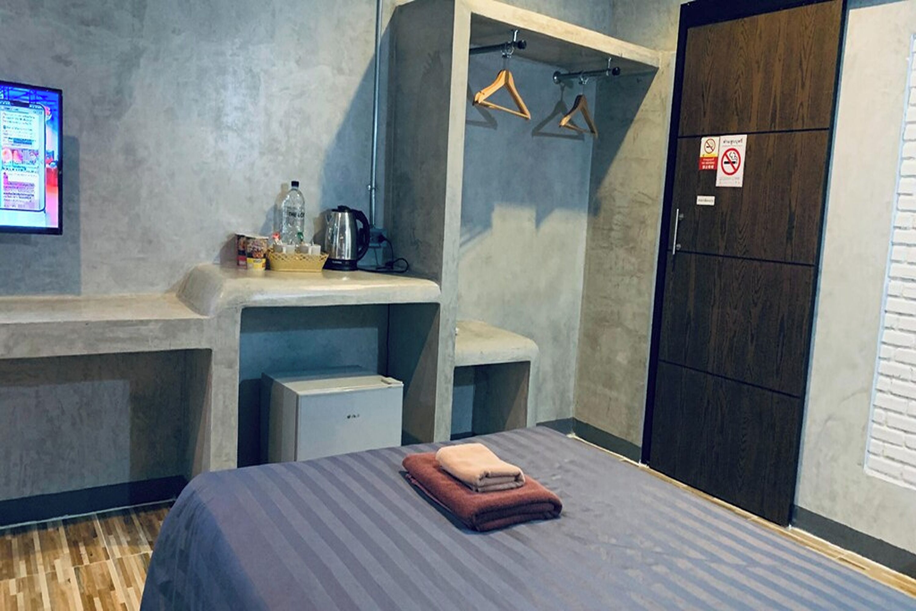 A hotel room with a bed, a desk, a small cabinet, a wardrobe, and a TV on the wall.