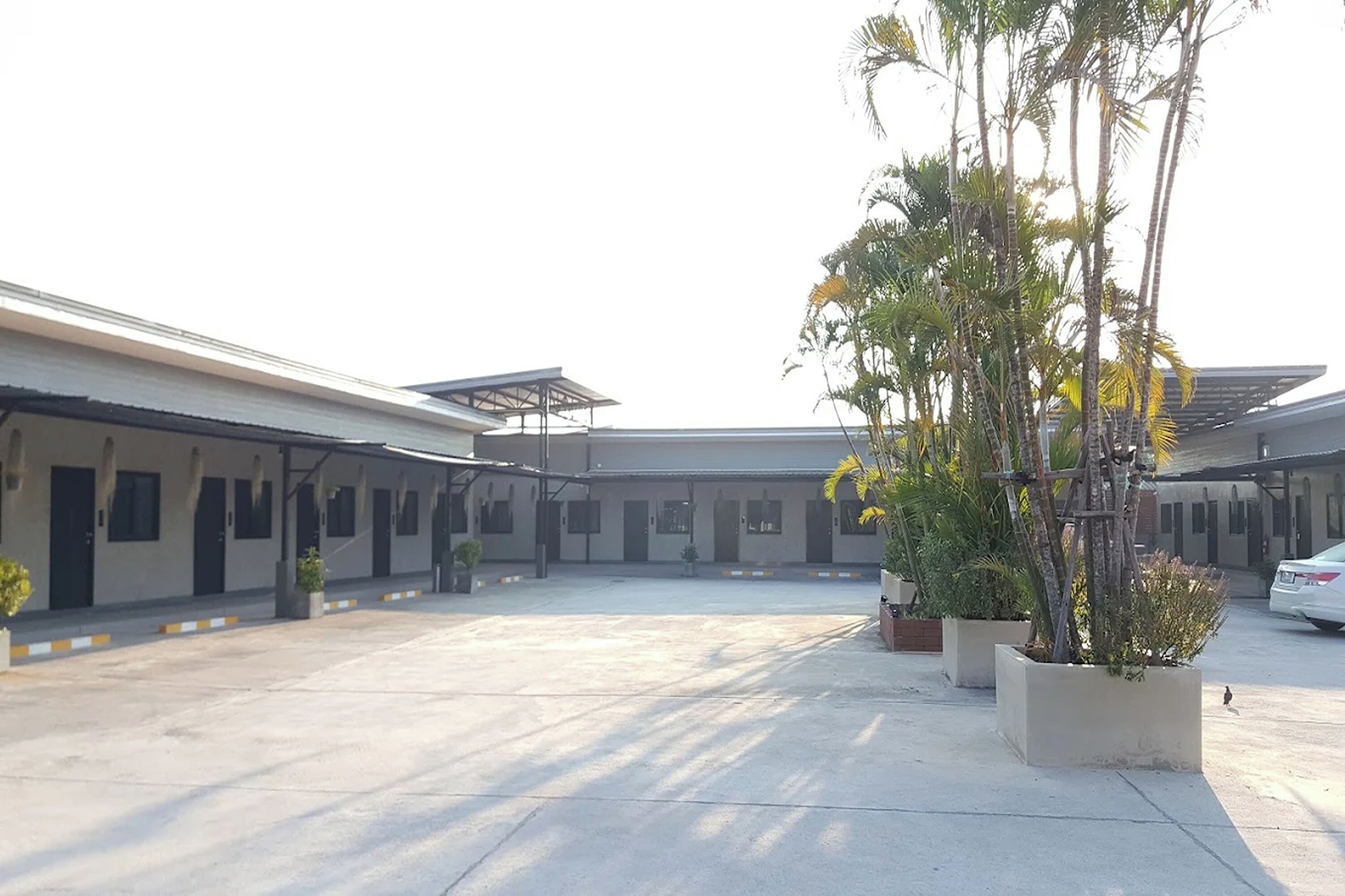 A spacious courtyard with a covered seating area, potted plants, and a car parked nearby.