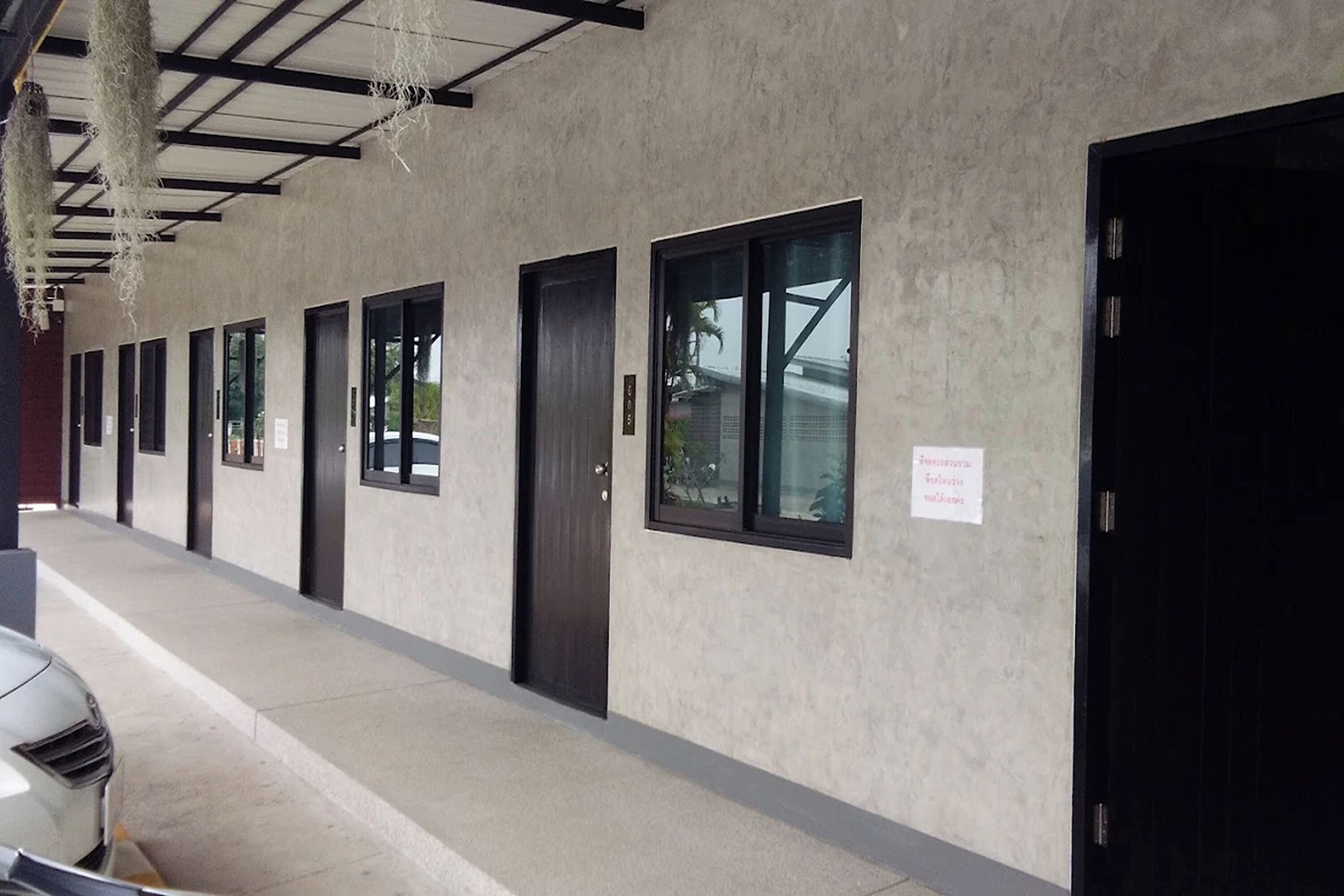 A row of hotel rooms with individual doors and windows, a concrete floor, and hanging decorations.