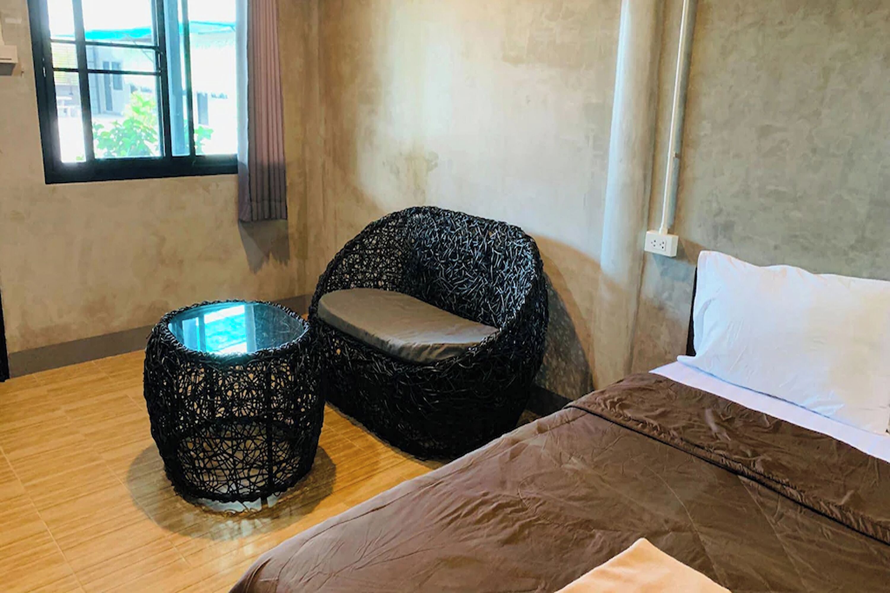 Una habitación con una cama, una silla de mimbre y una mesita.
