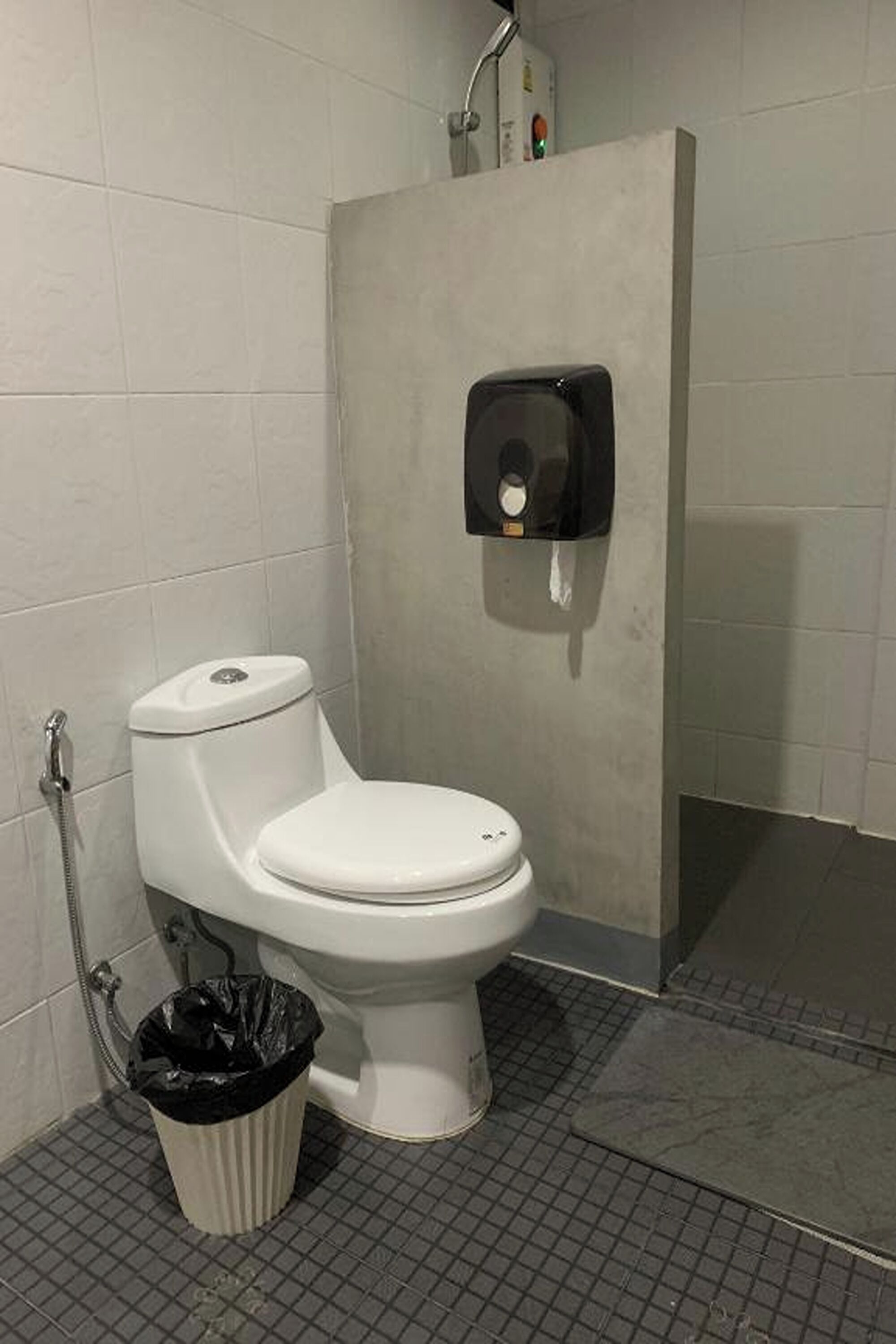 A small, enclosed bathroom with a toilet, a trash bin, and a hand dryer.