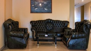 A living room with a black leather sofa, two armchairs, a coffee table, and a chandelier. - Grand Madani Hotel (Mataram)