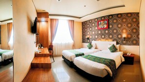 A hotel room with two beds, a wooden desk, a TV, and a patterned wall. - Grand Madani Hotel (Mataram)