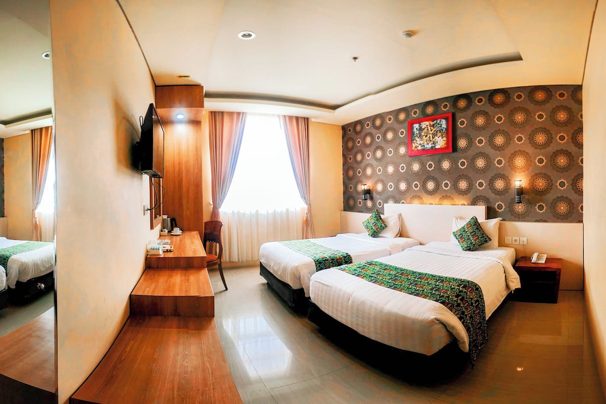 A hotel room with two beds, a wooden desk, a TV, and a patterned wall.