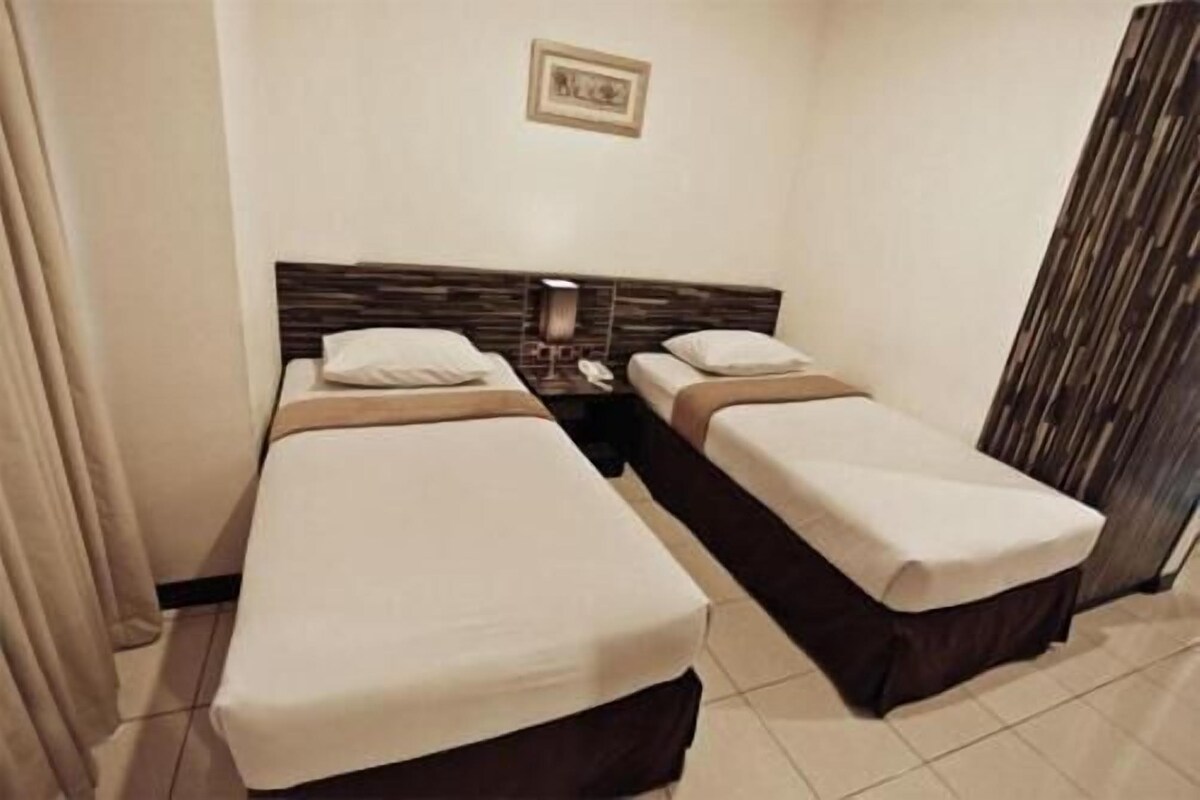 Una habitación de hotel con dos camas individuales, una mesita de noche con lámpara, teléfono y un cuadro en la pared.