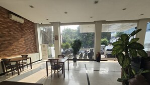 Et hotel lobby med en murstensvæg, møbler i træ, en stor stueplante og udsigt til gaden.