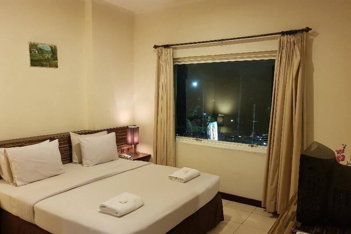 A hotel room with a bed, a TV, a nightstand, and a window with curtains.