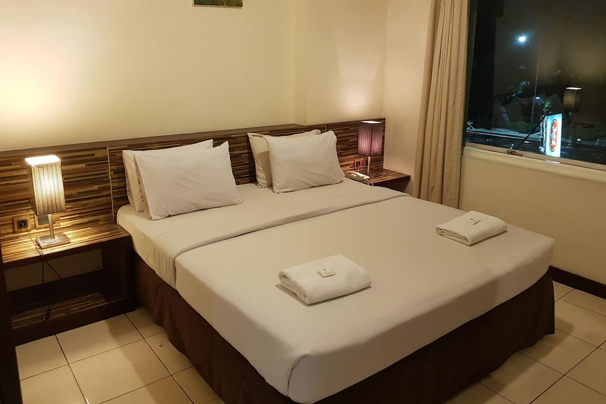 A neatly made bed with white linens, a bedside lamp, and a nightstand with a phone.