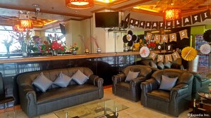 A hotel lobby with leather sofas, a glass coffee table, and a reception area with a TV and flower arrangements. - C & L Bay View Inn (Dumaguete)