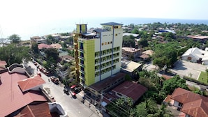 A multi-story building with a green facade and a flat roof, surrounded by residential houses and palm trees. - C & L Bay View Inn (Dumaguete)