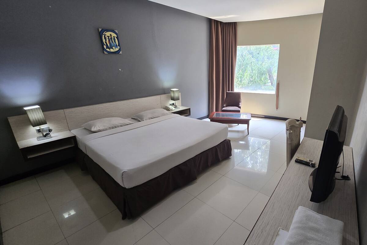 A hotel room with a large bed, a nightstand, a desk, a chair, a TV, and a window with curtains.