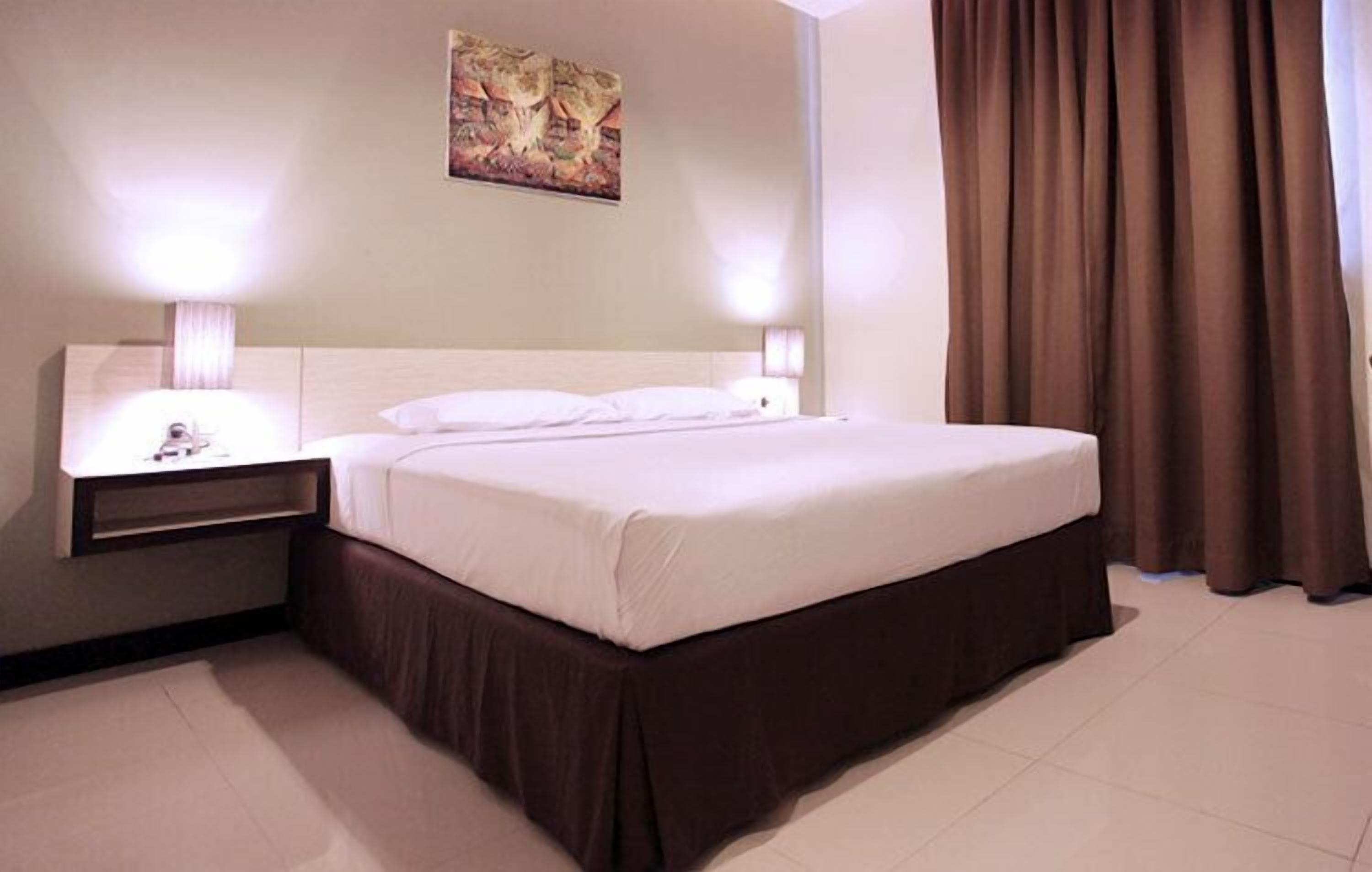 A hotel room with a large bed, two bedside tables with lamps, a painting on the wall, and a curtain.