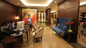 Un vestíbulo de hotel con una recepción, una computadora, varias sillas, un sofá y una estantería.