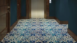 Un pasillo con alfombra estampada, paredes de madera y una puerta que da a un ascensor.