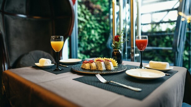 Una mesa servida con comida, dos bebidas y un florero con flores.