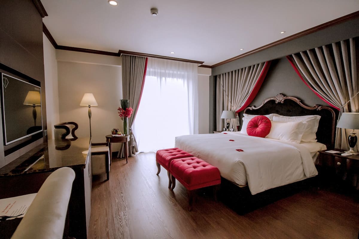 Une chambre d’hôtel avec un grand lit, un bureau, une chaise, une télévision et une fenêtre avec des rideaux.