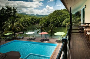A pool area with a view of a lake and mountains, surrounded by palm trees and outdoor seating. - Pechmaneekan Beach Resort (Sai Yok)