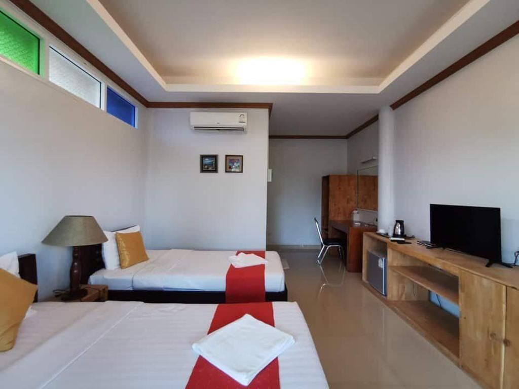 A hotel room with two beds, a desk, a television, and an air conditioning unit.