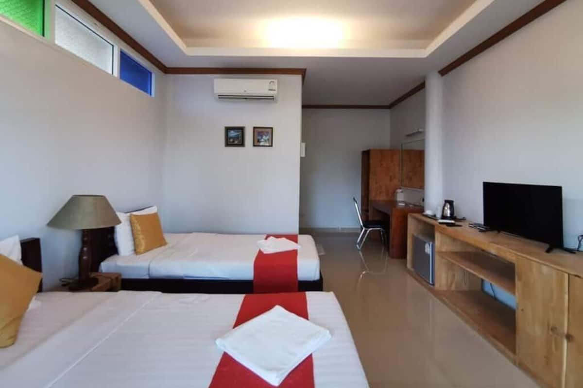 A hotel room with two beds, a desk, a television, and an air conditioning unit.