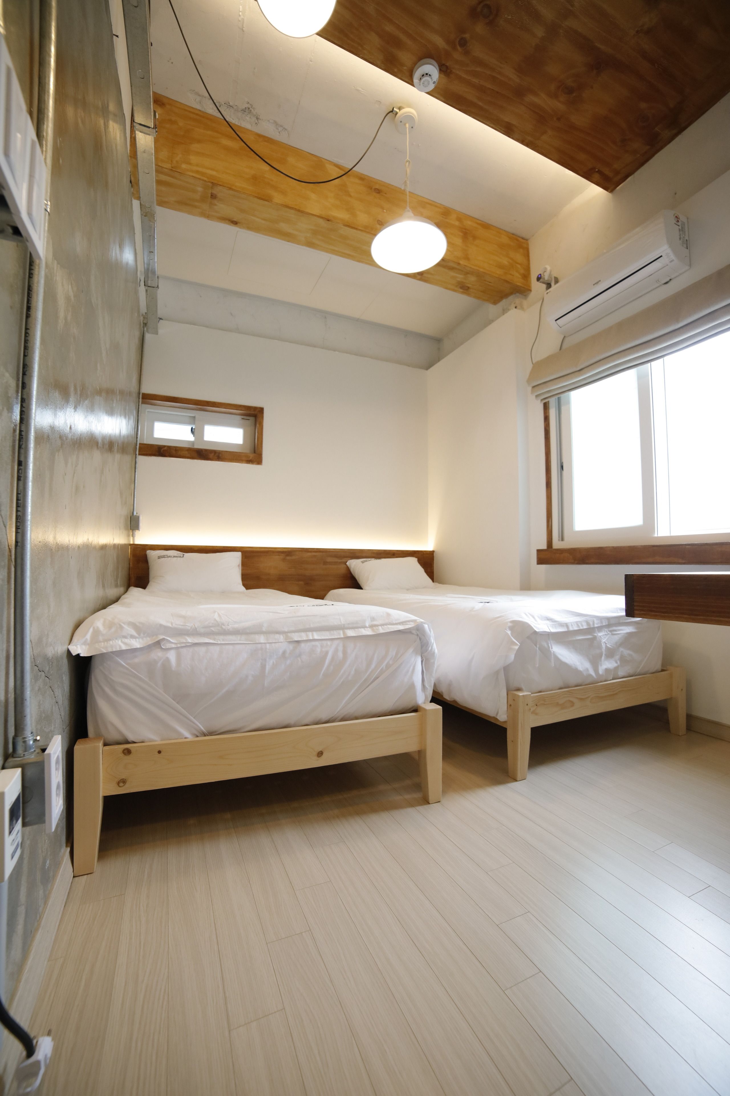 Quarto com duas camas de madeira, teto de madeira e janela que proporciona iluminação natural.