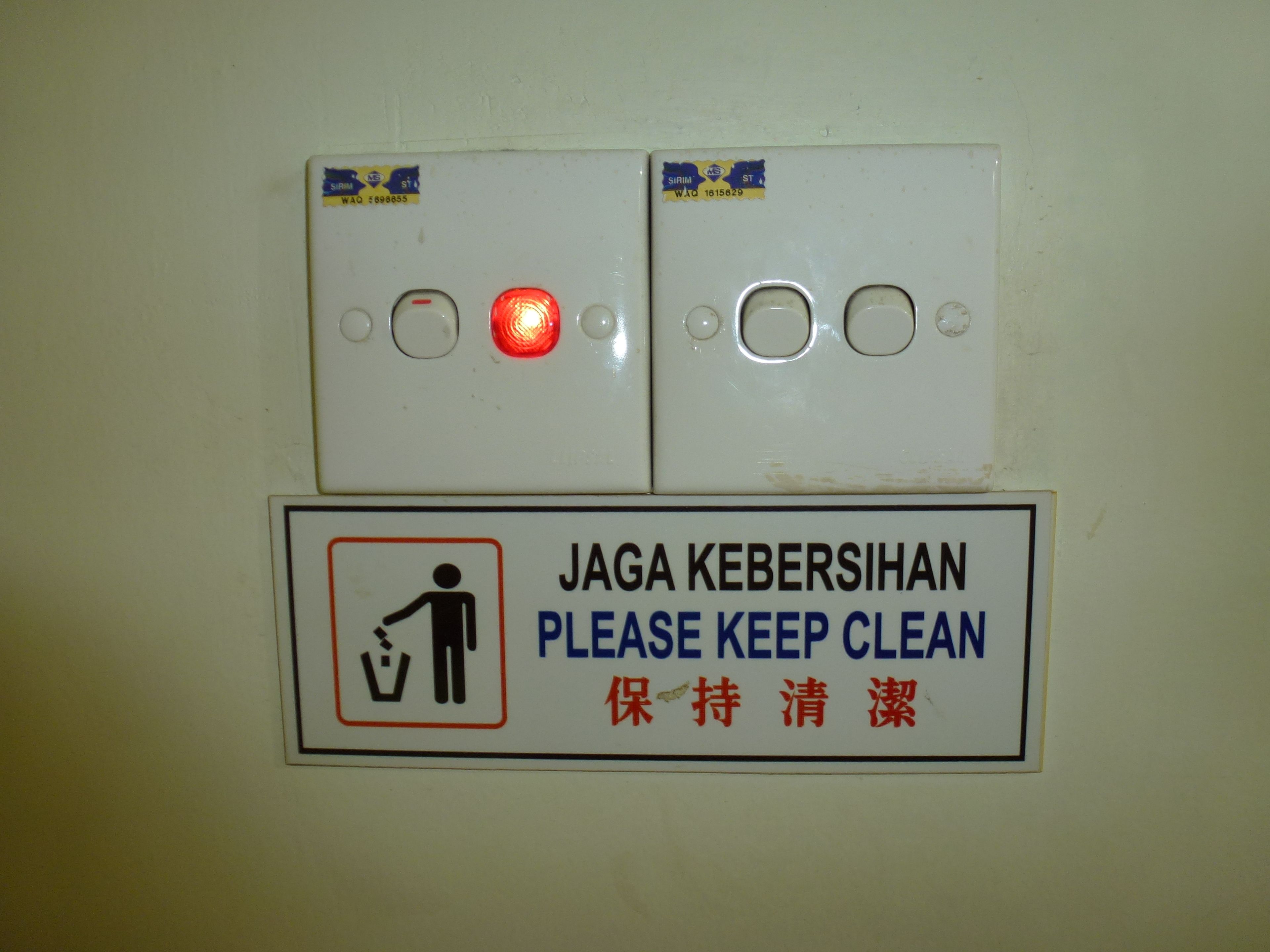 A wall-mounted light switch with a red light indicator and a sign below instructing to keep the area clean.