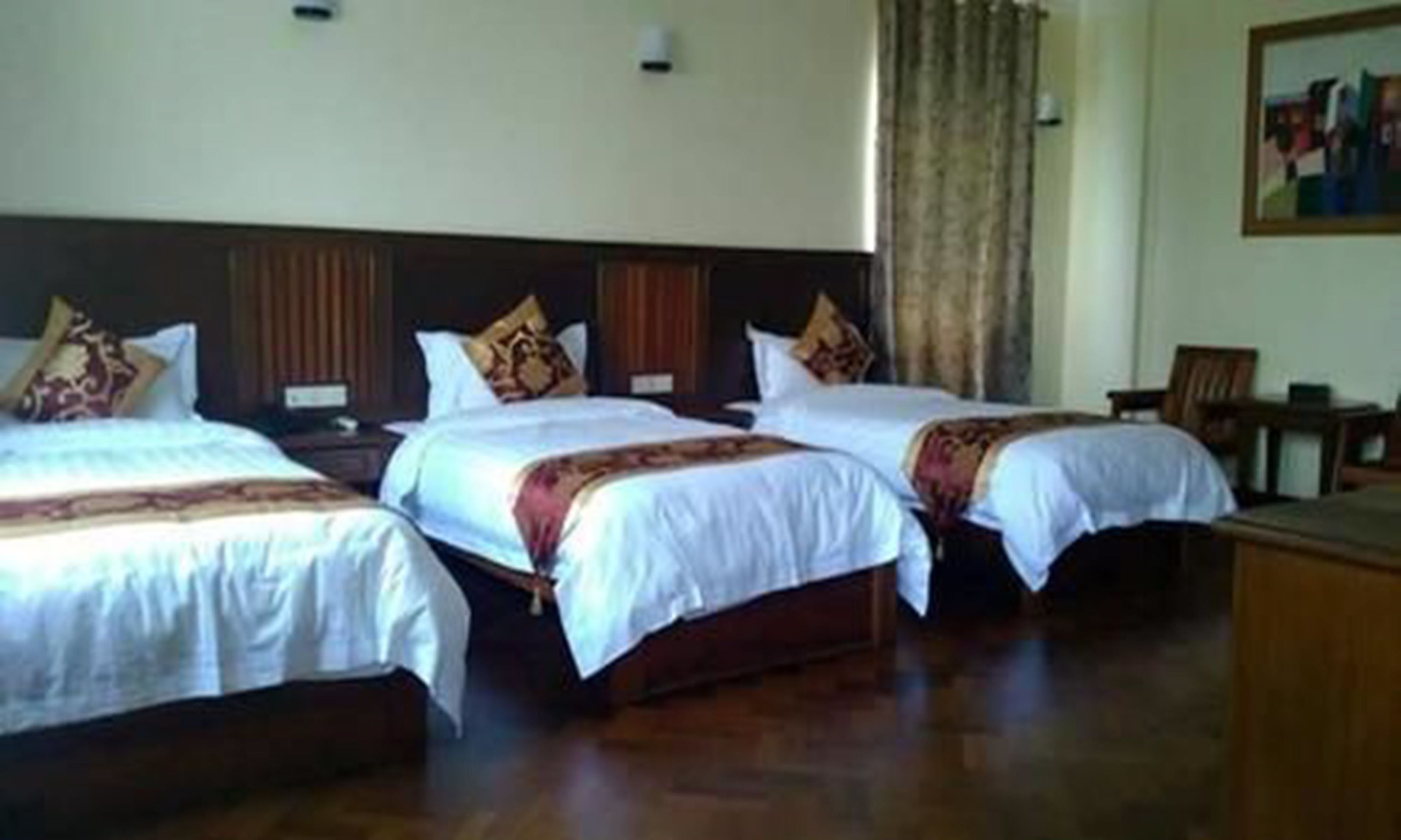 A hotel room with three beds, wooden headboards, and a painting on the wall.