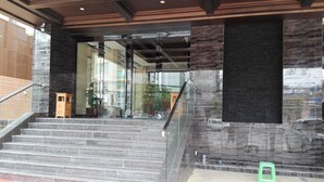 Una escalera conduce a la entrada de un edificio, con una puerta de vidrio, un taburete verde y una alfombra roja.