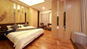 Habitación de hotel con una cama grande, suelo de madera, un escritorio con silla, una mesita y un refrigerador.