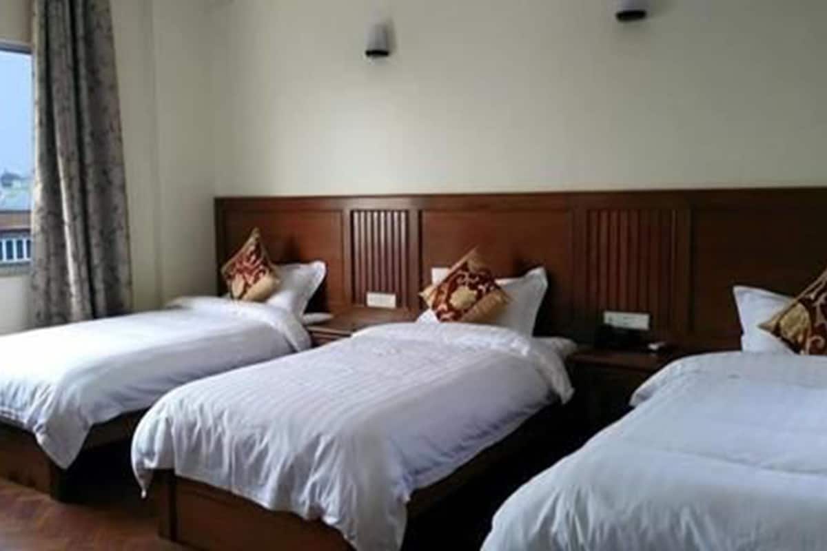 A hotel room with three single beds, each with a wooden headboard and white bedding.