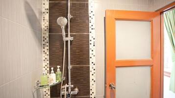 A bathroom with a shower, a glass shelf with toiletries, and a wooden door.