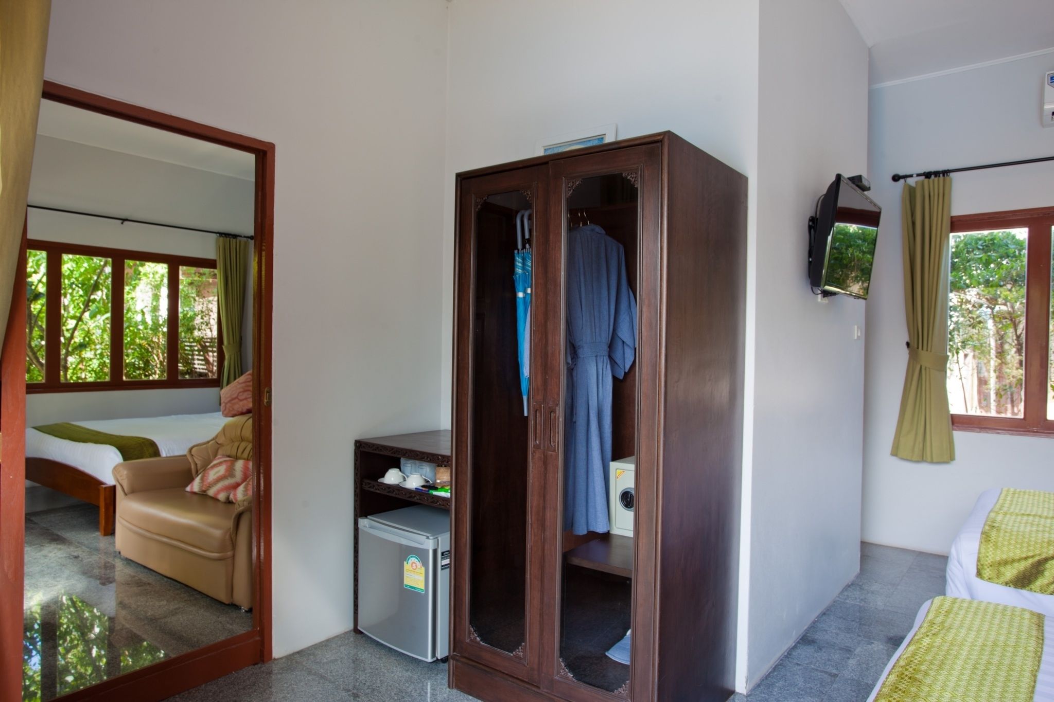 A bedroom with a bed, a wardrobe, a small desk with a computer, and a TV mounted on the wall.
