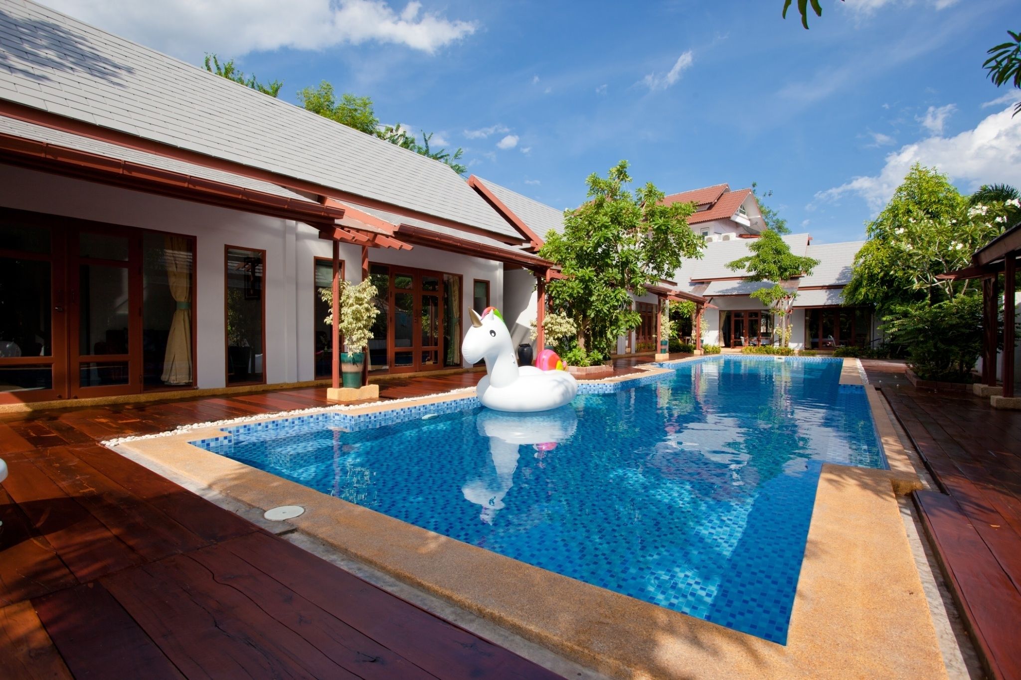 A swimming pool with a swan float, surrounded by wooden deck and potted plants.