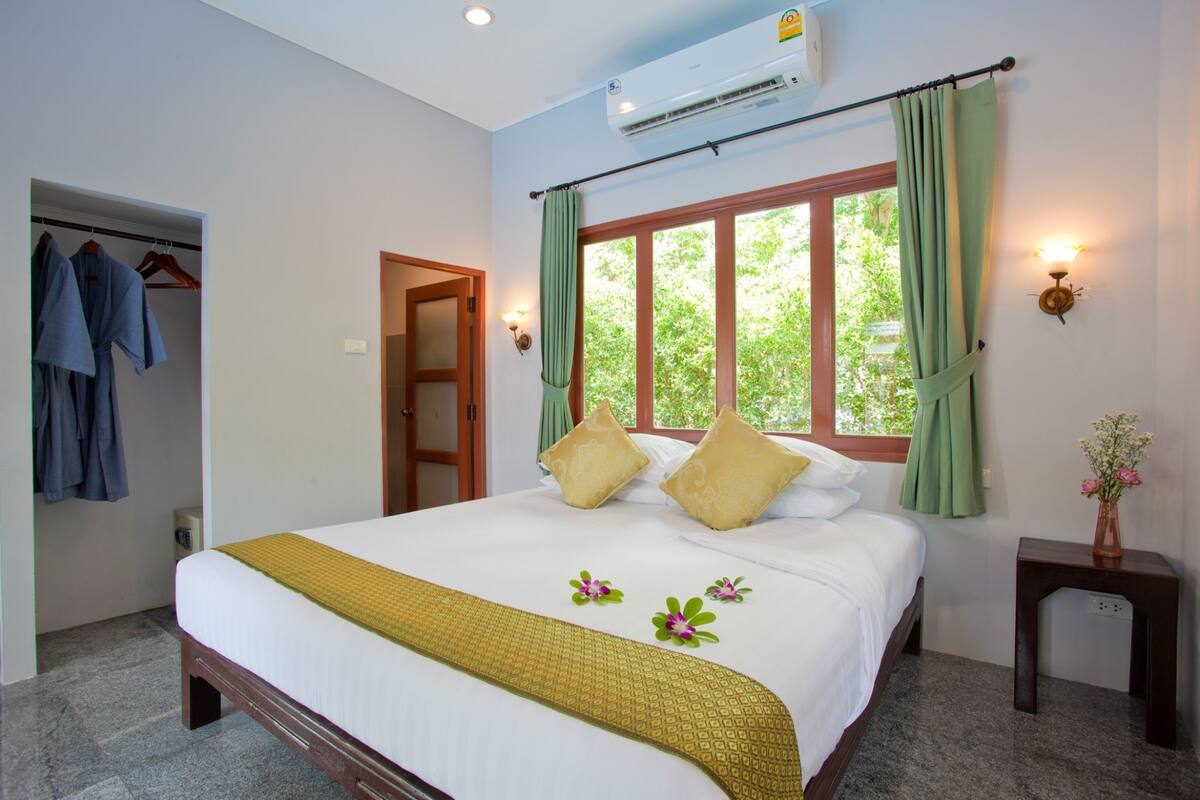 A neatly made bed with a white and yellow bedspread, two pillows, and a green curtain over a window.