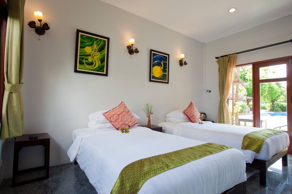A hotel room with two beds, a small table, wall-mounted lights, and artwork.