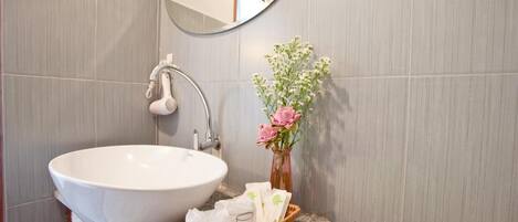Un baño con un lavamanos grande blanco, un espejo y un florero con flores.