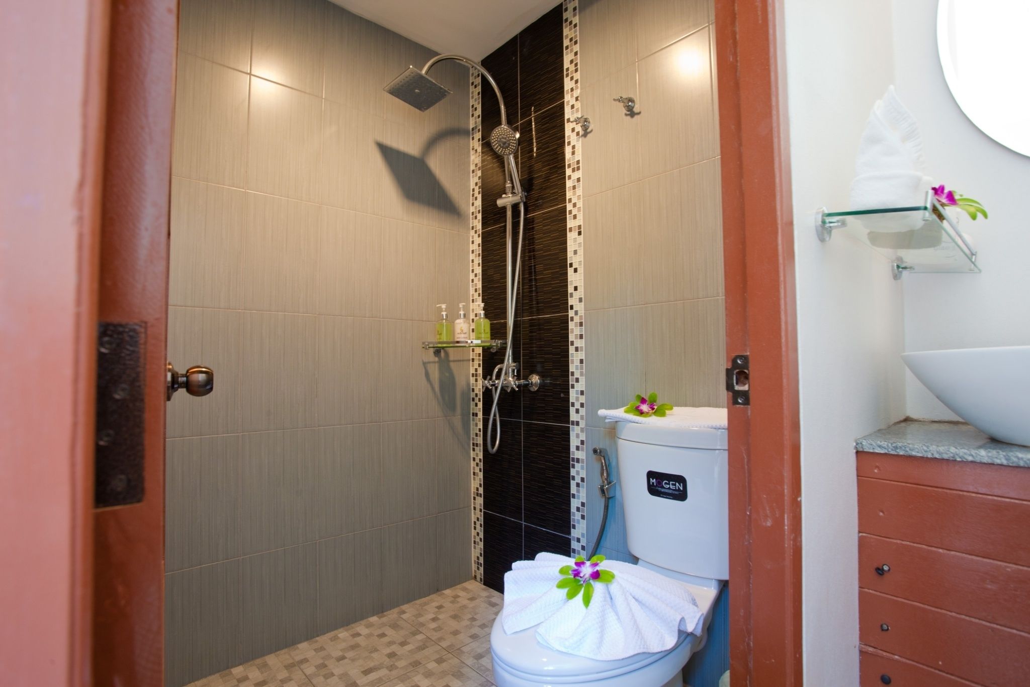 A bathroom with a shower, toilet, and a sink with a glass shelf.