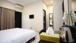 Une chambre d’hôtel comprenant un lit, une table de chevet avec une boîte de mouchoirs et une bouilloire, un téléviseur à écran plat et une porte avec un rideau.