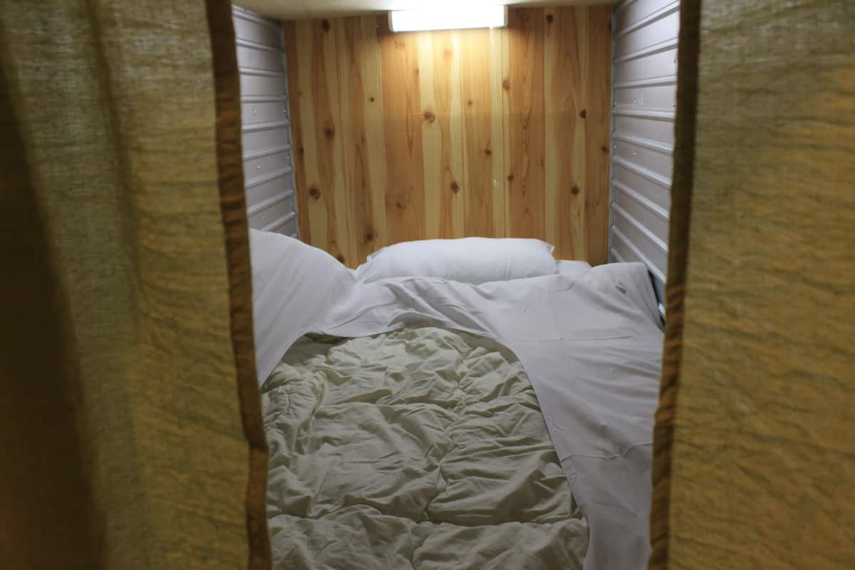 A small, narrow room with wooden walls and a bed with white bedding.